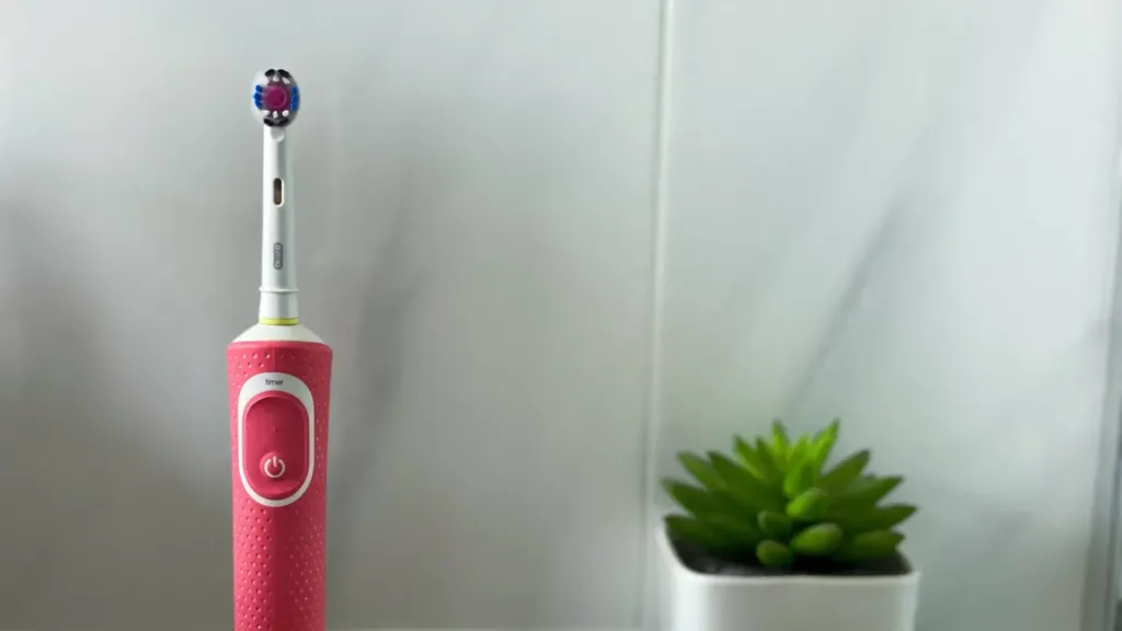 An electric toothbrush in a bathroom with a small green plant behind it